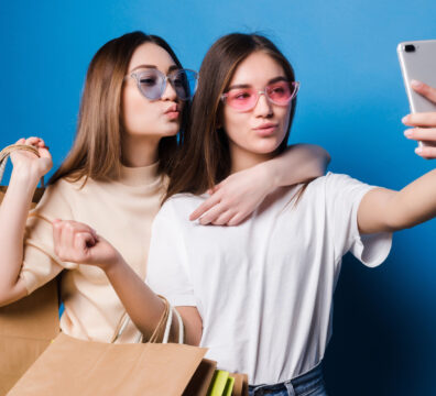 2 garotas segurando celular e fazendo pose com sacola de compras