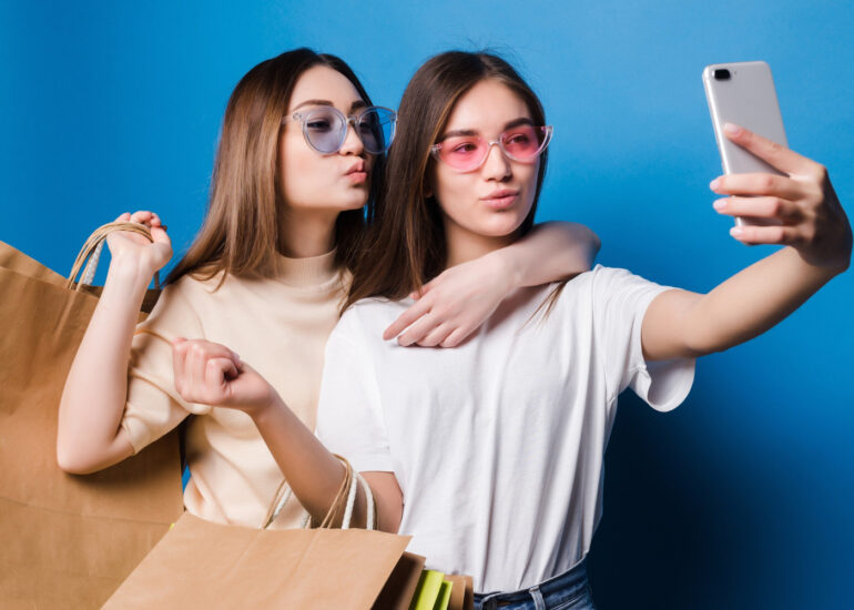 2 garotas segurando celular e fazendo pose com sacola de compras